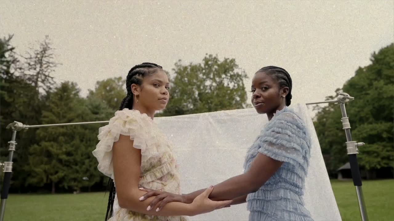 Two young women in gowns holding hands before a shimmering backdrop